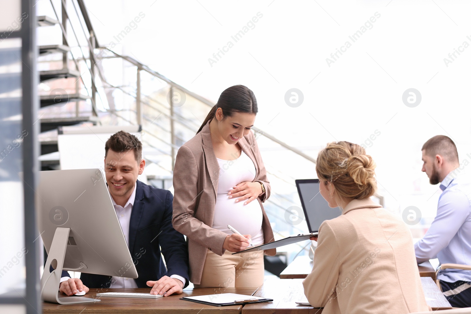 Photo of Young pregnant woman working with her employees in office