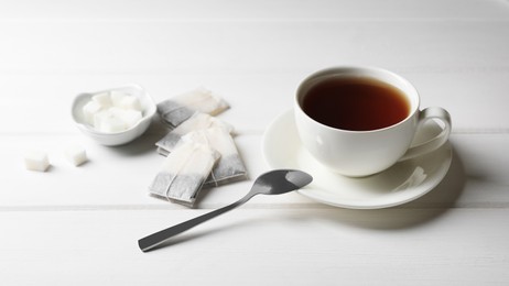 Tea bags and sugar near cup of hot drink on white wooden table. Space for text