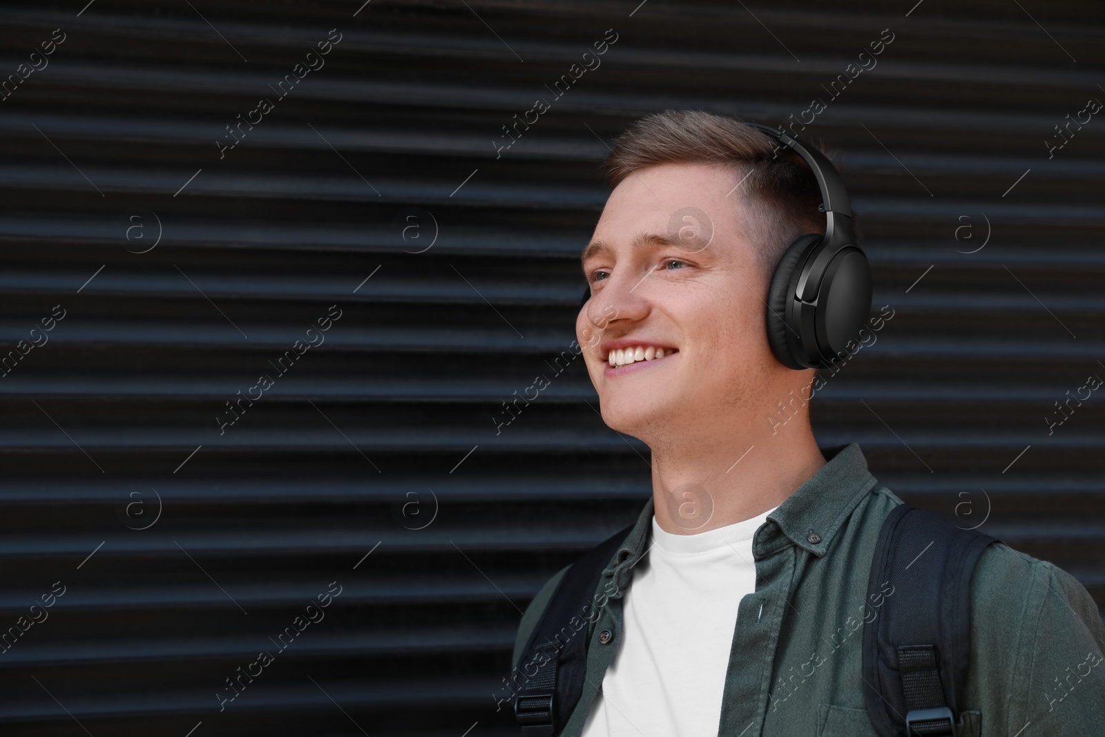 Photo of Smiling man wearing headphones near shutters outdoors. Space for text