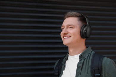 Smiling man wearing headphones near shutters outdoors. Space for text