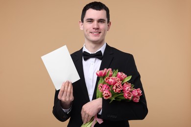 Photo of Happy young man with beautiful bouquet and greeting card on beige background