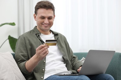 Photo of Happy man with credit card using laptop for shopping online on sofa at home
