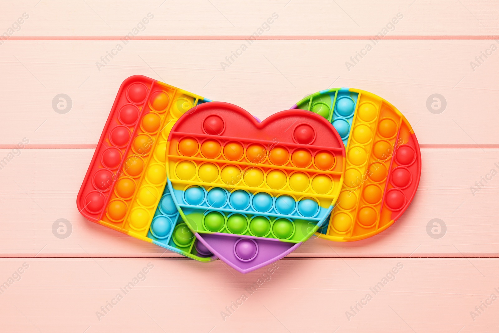 Photo of Rainbow pop it fidget toys on pink wooden table, flat lay