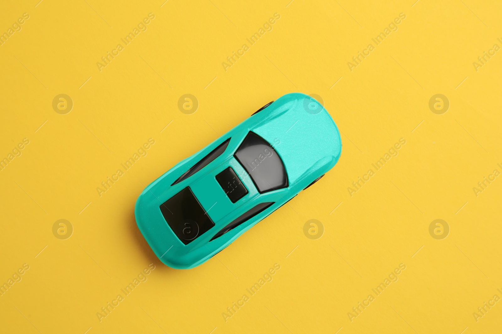 Photo of One turquoise car on yellow background, top view. Children`s toy