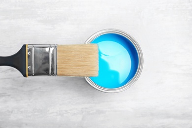 Photo of Can with blue paint and brush on light background, top view