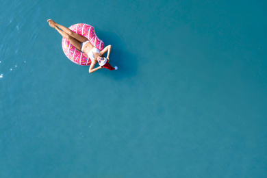 Young woman wearing Santa hat and bikini with inflatable ring in sea, top view. Christmas vacation