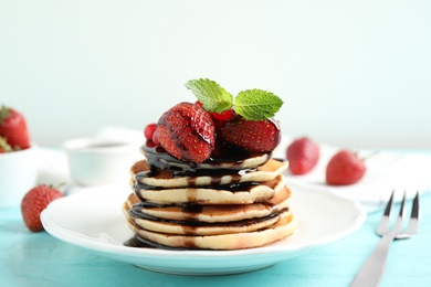 Photo of Delicious pancakes with fresh strawberries and chocolate syrup on light blue wooden table