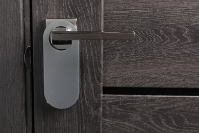 Photo of Closed wooden door with blank hanger on metal handle, closeup