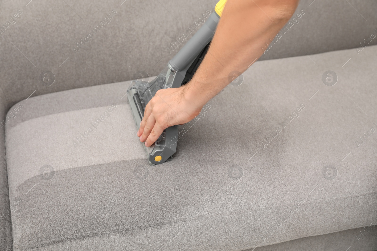 Photo of Janitor removing dirt from sofa with upholstery cleaner, closeup