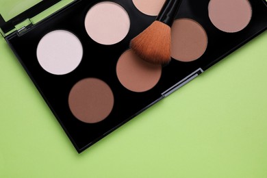 Photo of Colorful contouring palette with brush on light green background, top view. Professional cosmetic product