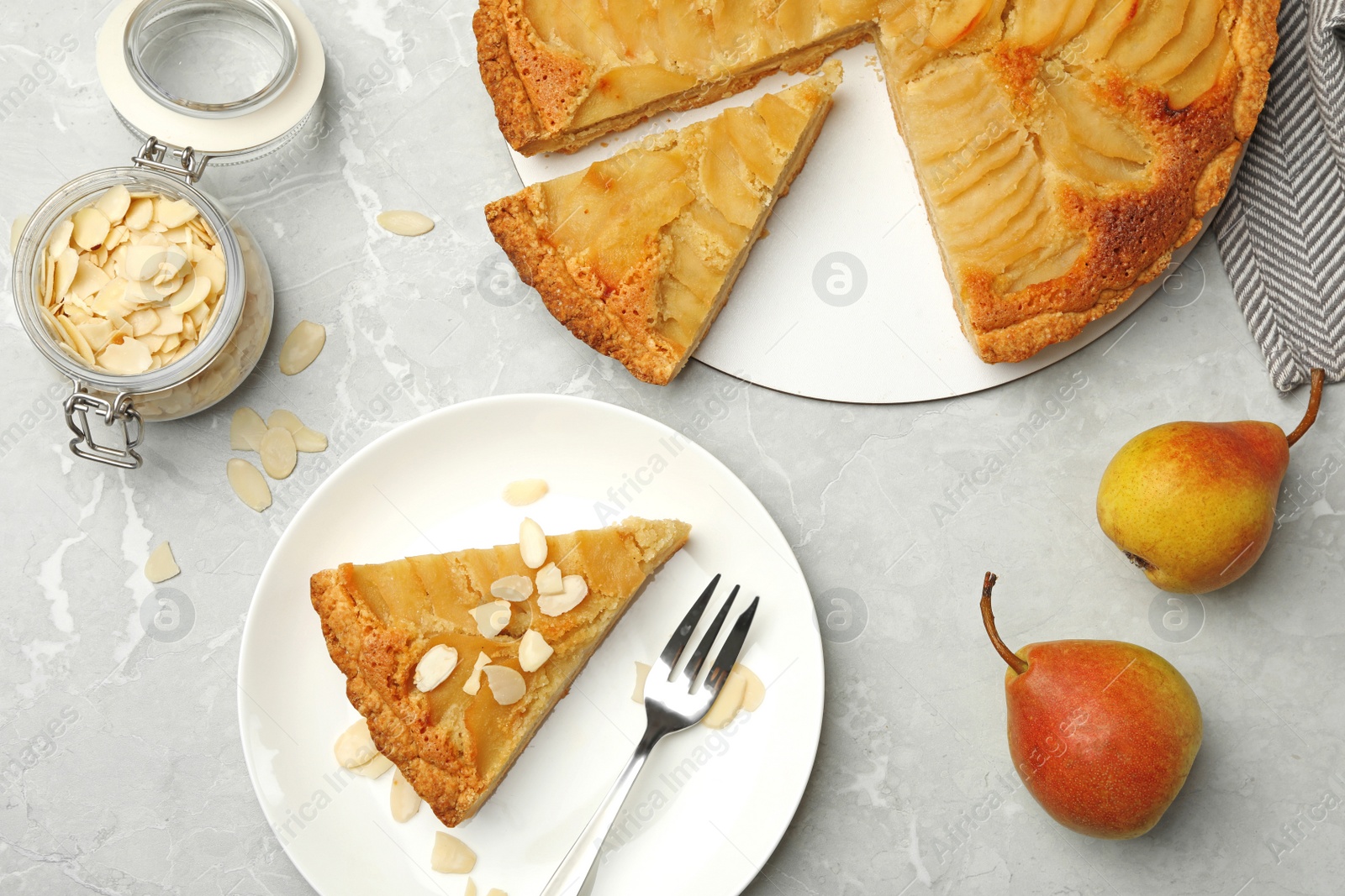 Photo of Cut delicious sweet pear tart and almond flakes on grey marble table, flat lay