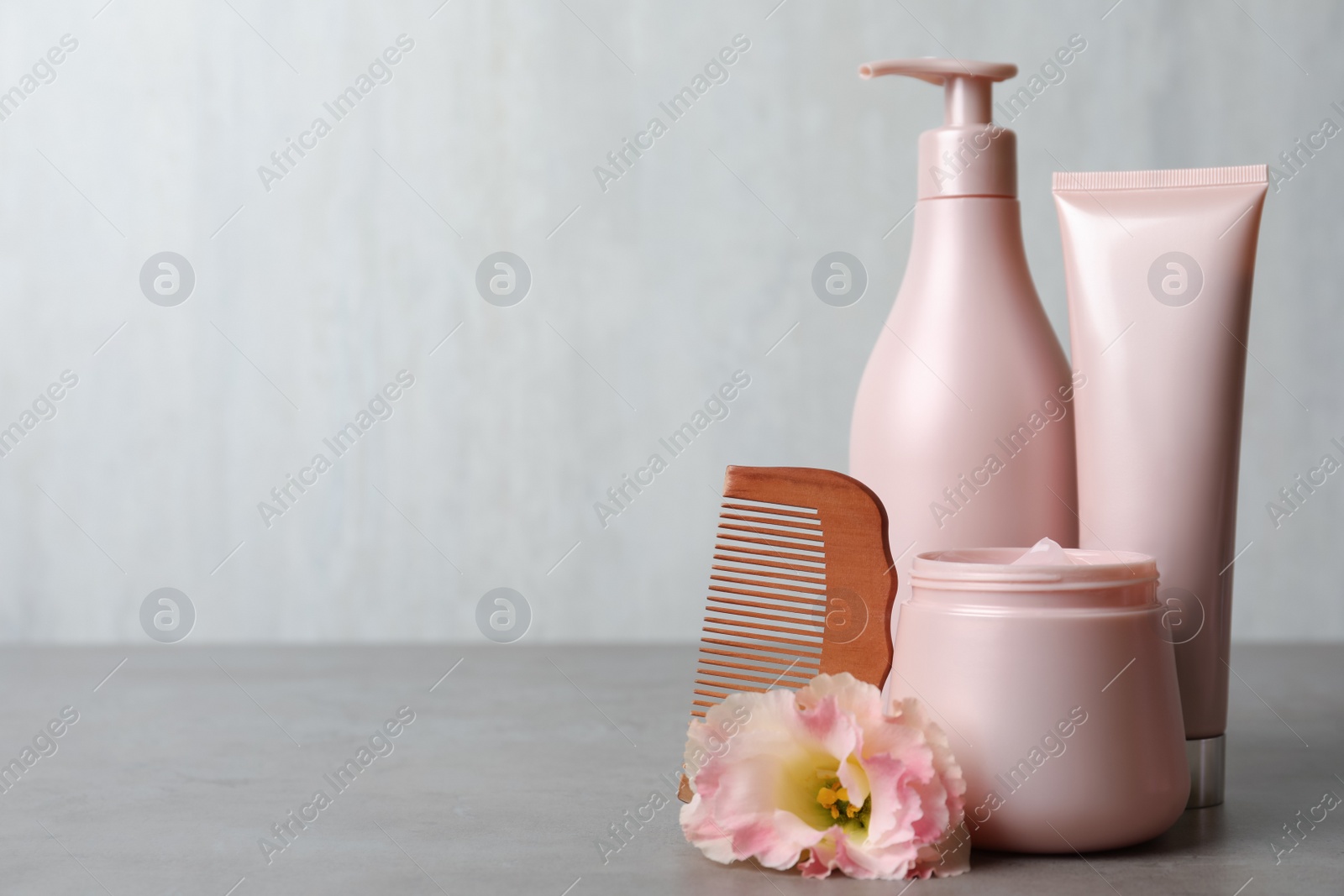 Photo of Different hair products, flower and wooden comb on grey table. Space for text