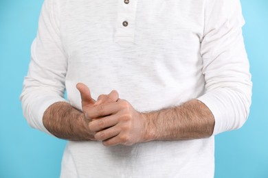 Photo of Man cracking his knuckles on light blue background, closeup. Bad habit