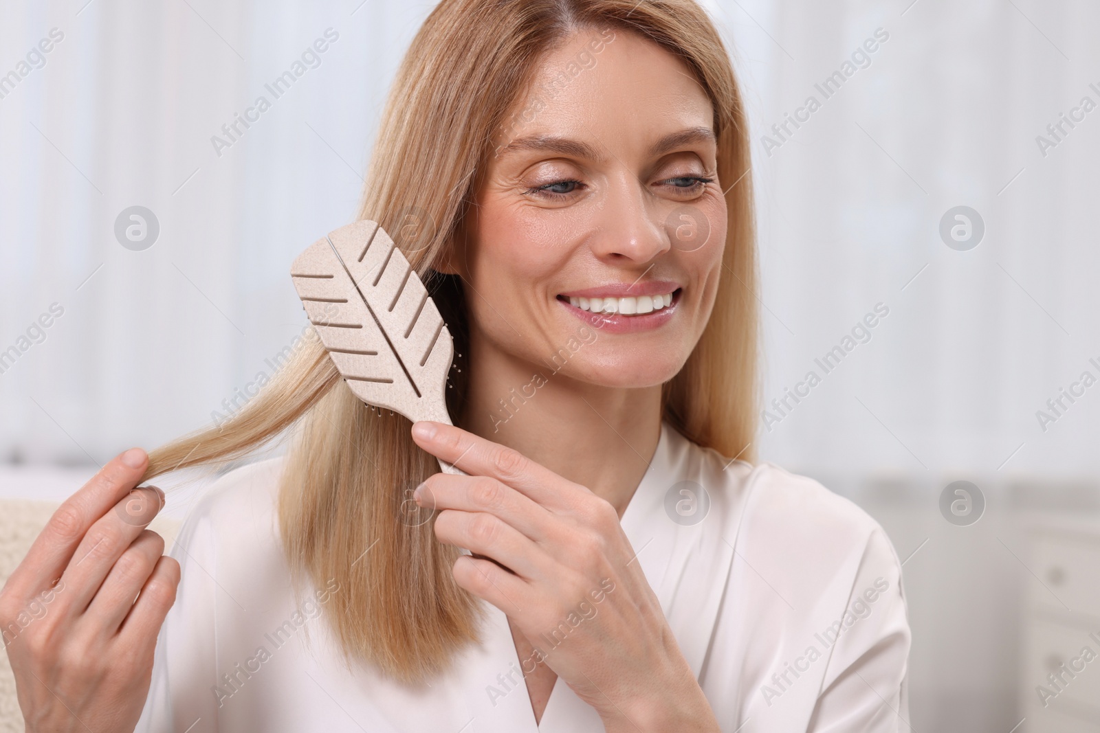 Photo of Beautiful happy woman brushing her hair in bedroom