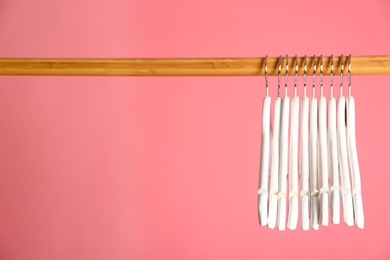 Photo of Empty clothes hangers on wooden rail against color background. Space for text