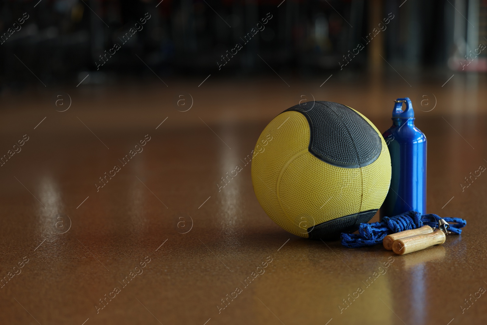 Photo of Medicine ball, bottle and skipping rope on floor in gym. Space for text