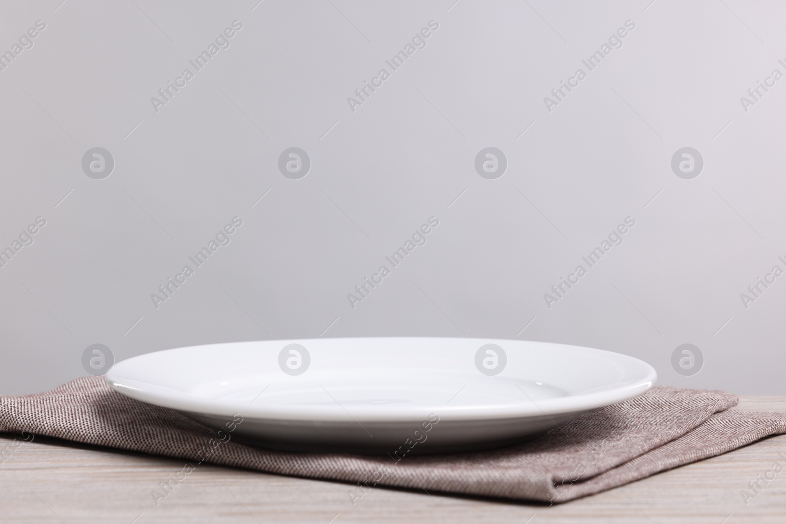 Photo of Empty ceramic plate on wooden table against light background, space for text