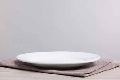 Photo of Empty ceramic plate on wooden table against light background, space for text