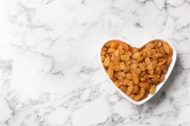 Photo of Heart shaped plate with raisins and space for text on marble background, top view. Dried fruit as healthy snack