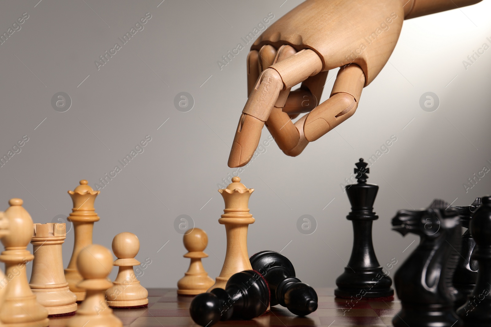 Photo of Robot moving chess piece on board against light grey background, closeup. Wooden hand representing artificial intelligence