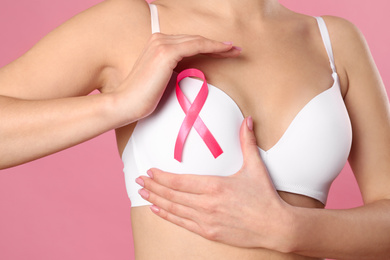 Woman with pink ribbon on color background, closeup. Breast cancer awareness