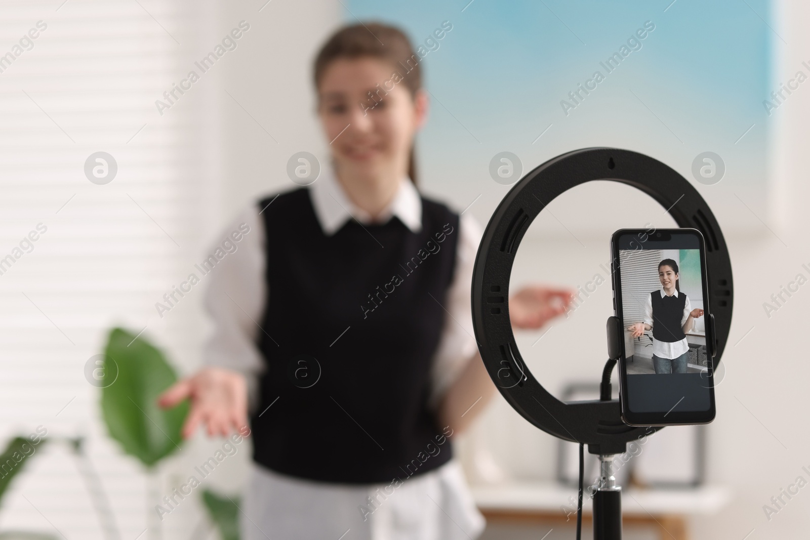 Photo of Teenage blogger explaining something while streaming at home, focus on smartphone