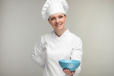 Photo of Happy chef in uniform holding bowl on grey background