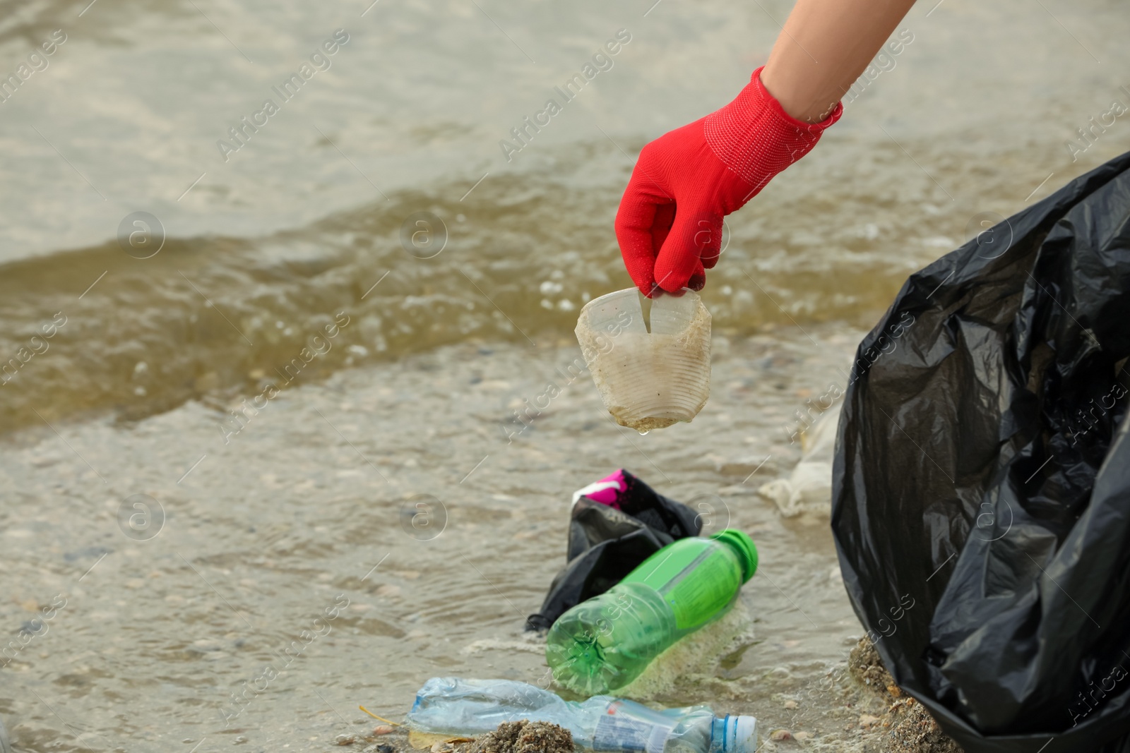 Photo of Woman in gloves with trash bag collecting garbage on beach, closeup