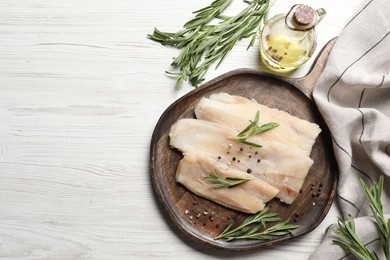 Photo of Raw cod fish, rosemary, oil and spices on white wooden table, flat lay. Space for text