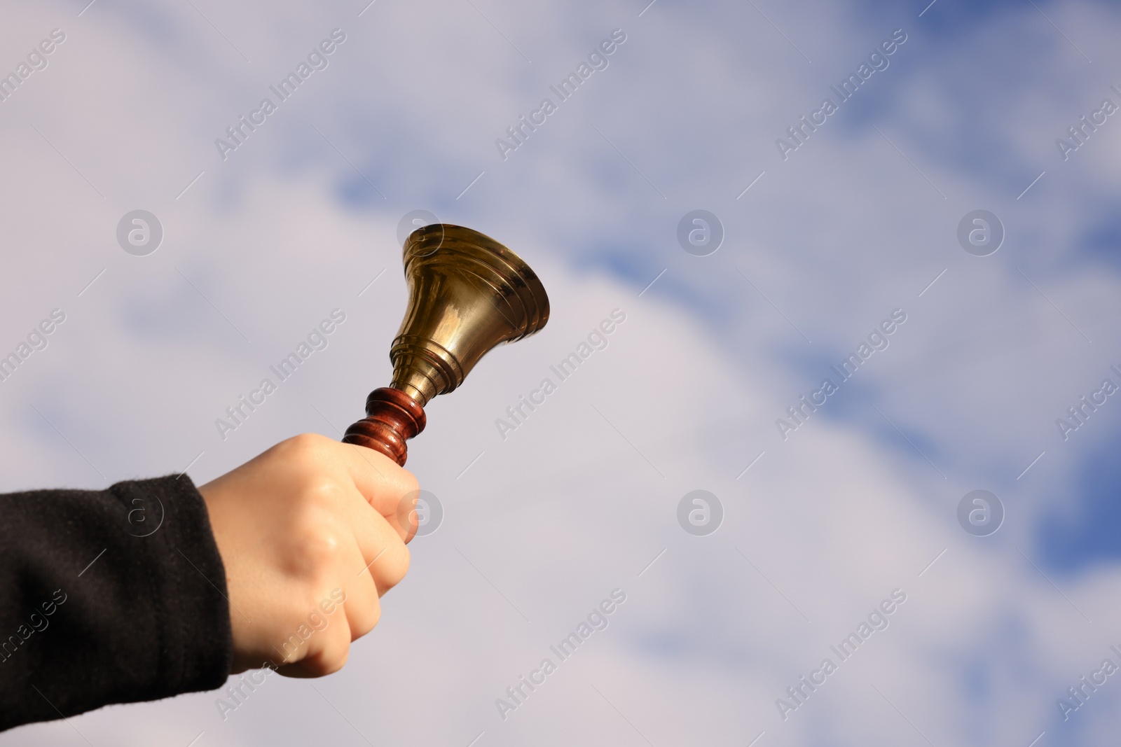 Photo of Pupil with school bell against cloudy sky, closeup. Space for text