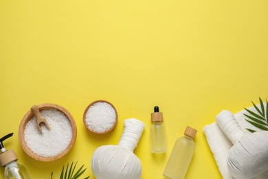 Photo of Beautiful spa composition with herbal massage bags and different care products on yellow background, flat lay. Space for text