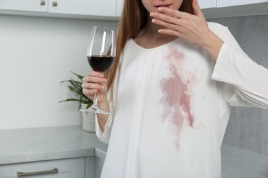 Embarrassed woman with stain on her clothes and glass of wine indoors, closeup