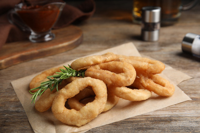 Photo of Pile of delicious crunchy fried onion rings and rosemary on wooden table