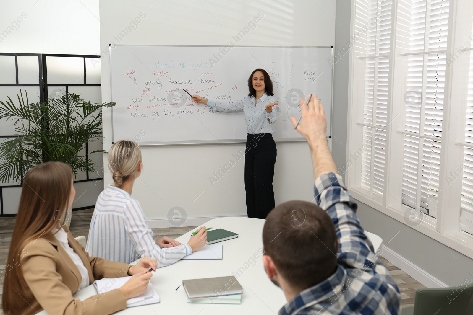 Photo of English teacher giving lesson near whiteboard in classroom