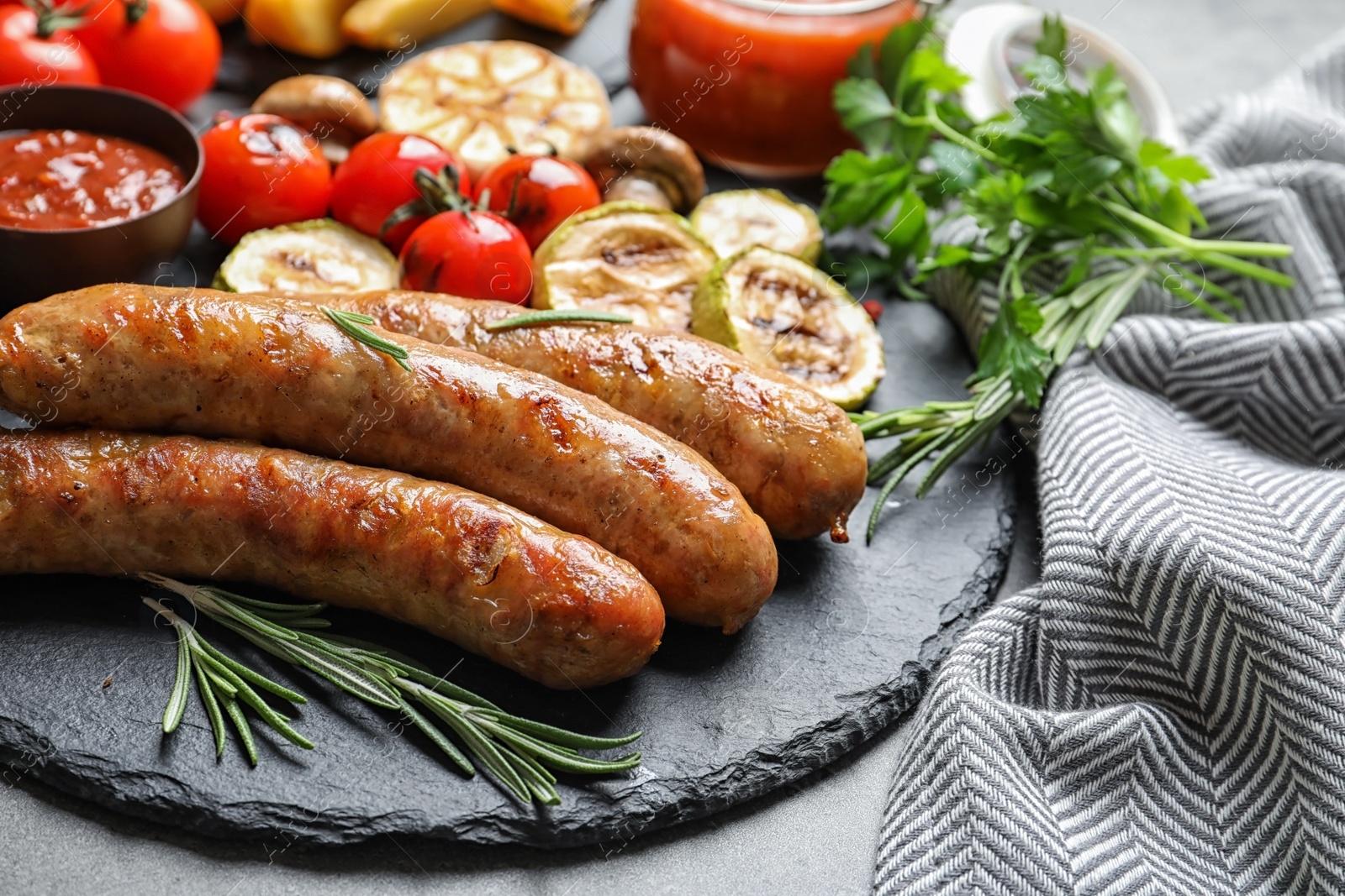 Photo of Slate plate with delicious sausages and vegetables served for barbecue party on gray table