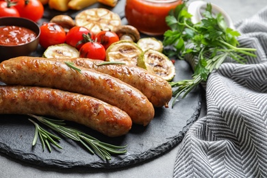 Slate plate with delicious sausages and vegetables served for barbecue party on gray table