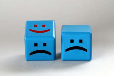 Image of Light blue cubes with sad and happy faces on light grey background