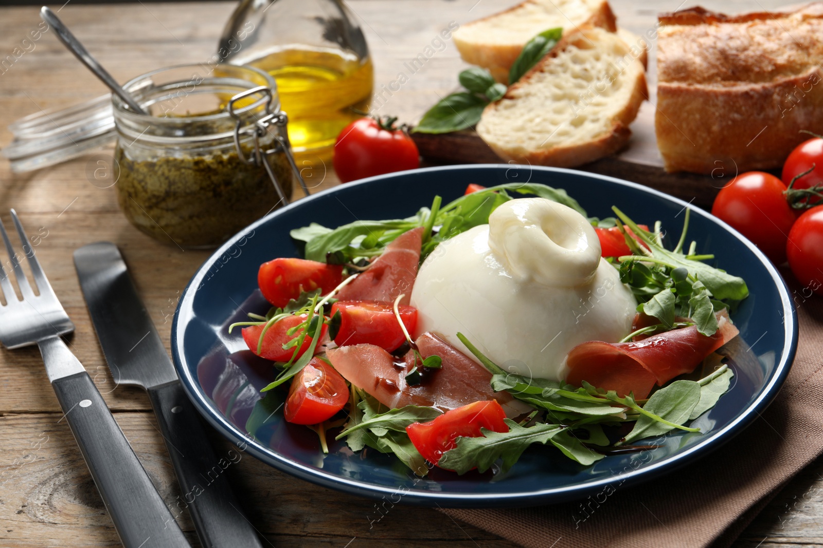 Photo of Delicious burrata salad with tomatoes, prosciutto and arugula served on wooden table