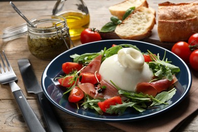 Photo of Delicious burrata salad with tomatoes, prosciutto and arugula served on wooden table