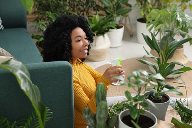 Photo of Happy woman spraying beautiful potted houseplant with water at home