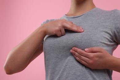 Photo of Woman doing breast self-examination on pink background, closeup