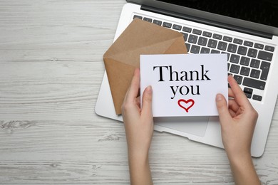 Woman holding card with phrase Thank You ar white wooden table, top view. Space for text