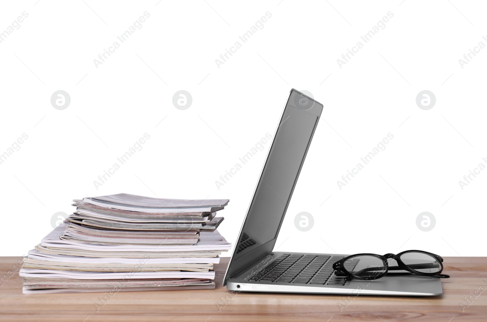 Photo of Laptop, glasses and stack of magazines on wooden table