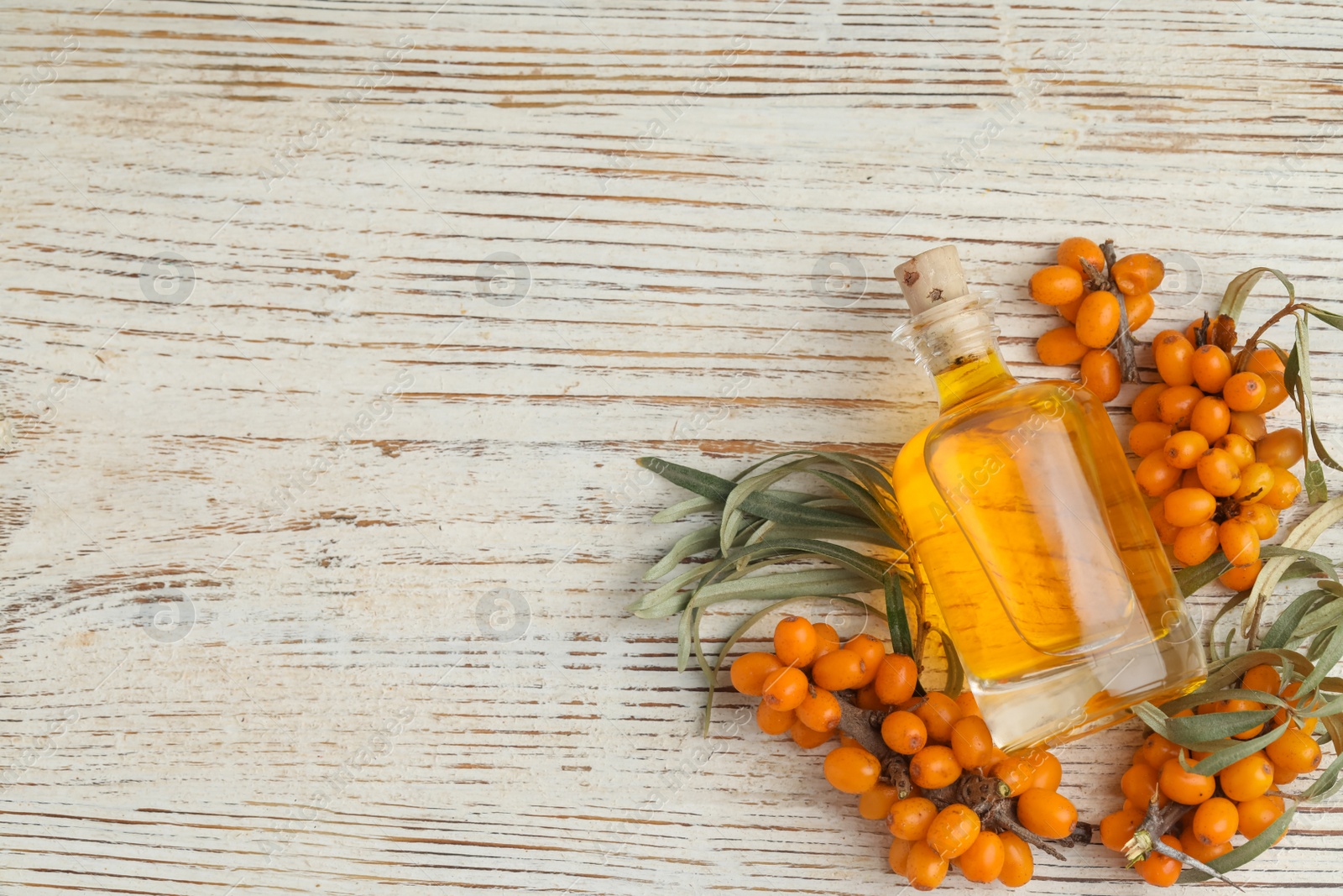 Photo of Natural sea buckthorn oil and fresh berries on white wooden table, flat lay. Space for text