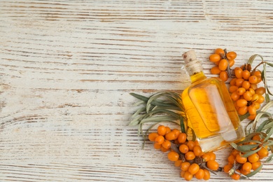 Natural sea buckthorn oil and fresh berries on white wooden table, flat lay. Space for text