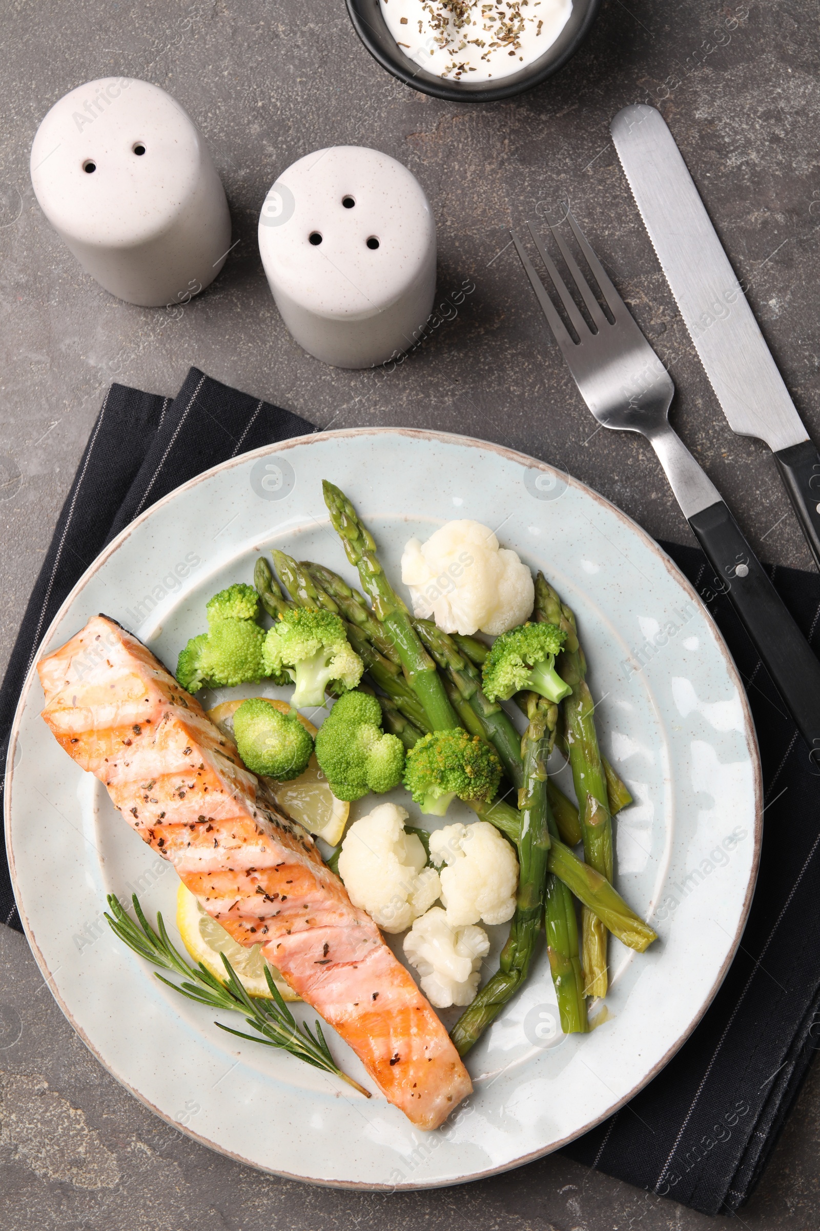 Photo of Healthy meal. Piece of grilled salmon, vegetables, asparagus and rosemary served on grey textured table, flat lay