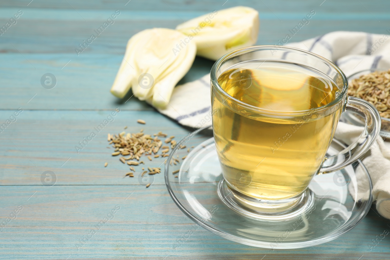 Photo of Aromatic fennel tea, seeds and fresh vegetable on light blue wooden table, closeup. Space for text