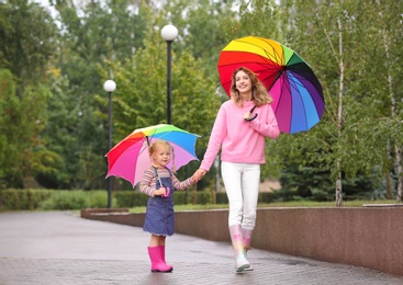 Happy mother and daughter with bright umbrellas walking in park