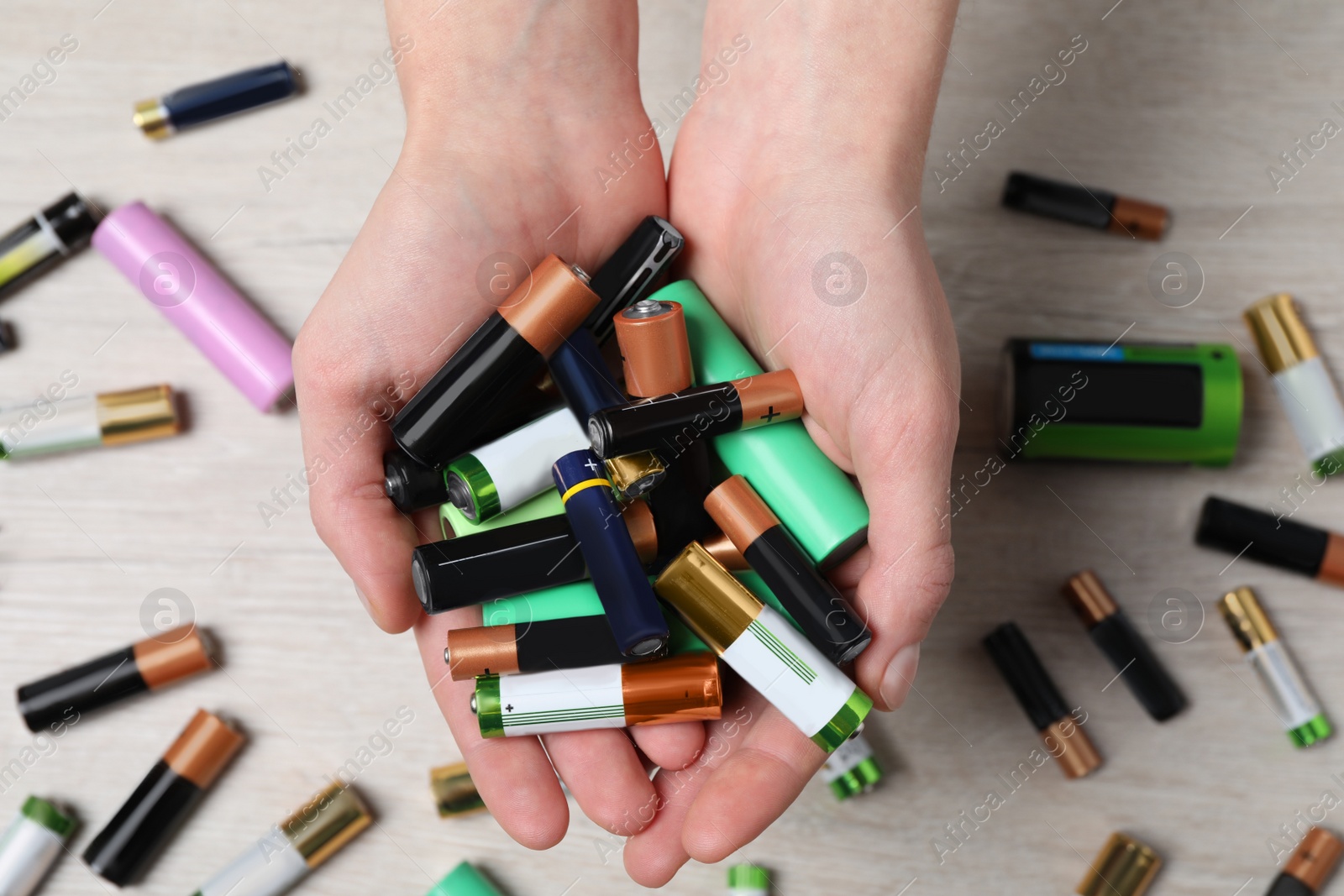 Image of Woman holding many used electric batteries in her hands over white table, closeup