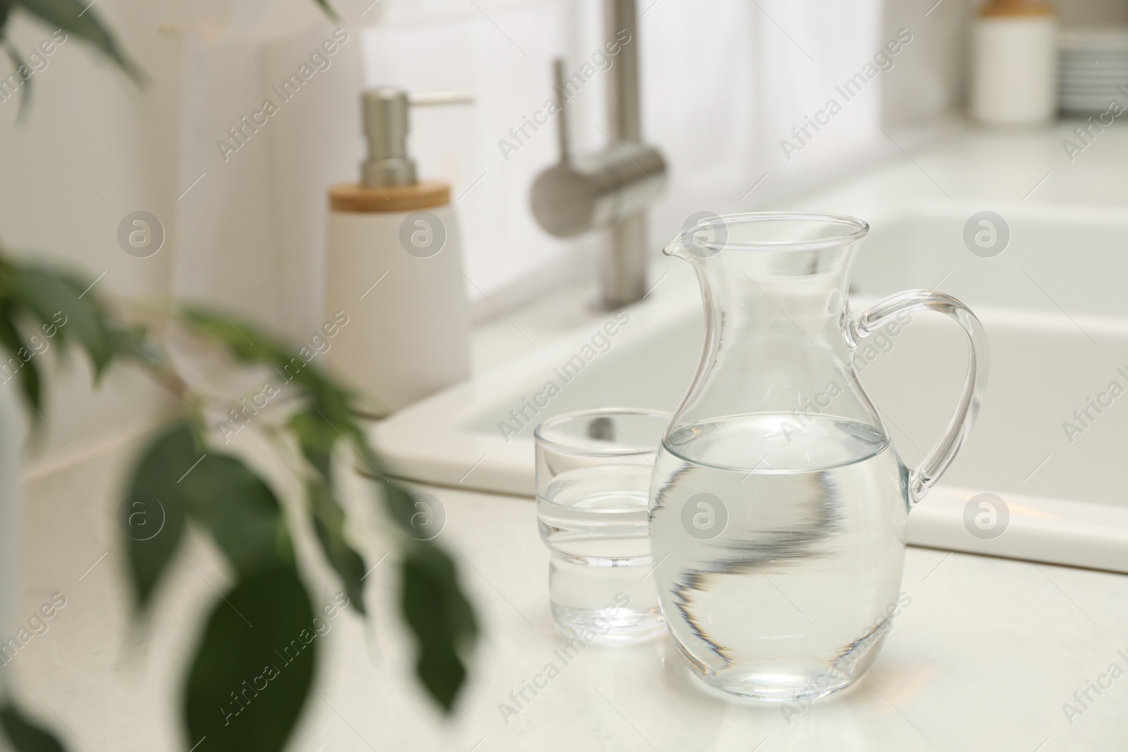 Photo of Jug and glass with clear water on white table in kitchen